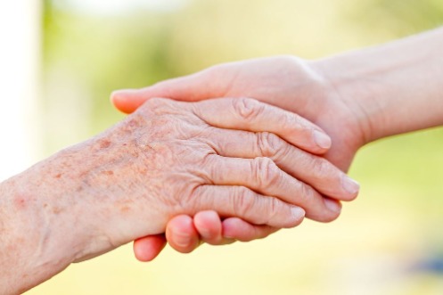 Eine jünger wirkende Hand umfasst die Hand einer älteren Person.
